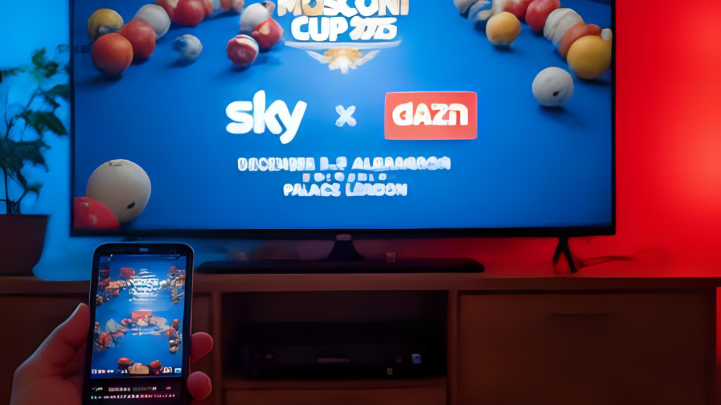 A person watching the Mosconi Cup 2025 live on a TV screen with Sky Sports and DAZN logos displayed, holding a smartphone showing the event stream, in a dimly lit room with red and blue lighting and popcorn on the table.